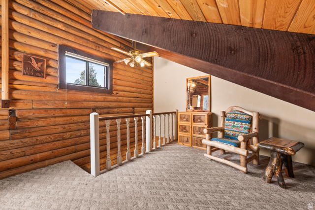 4725 Pine Ridge Road Evanston, UT 82930 - Photo 49 of 82 Loft area featuring log walls, an exposed wood beam ceiling, a ceiling fan with light fixture, and plush carpet flooring
