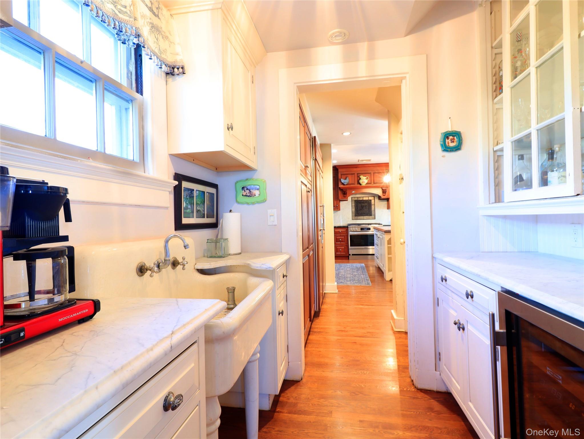 11-20 Shore Road Queens, NY 11363 - Photo 29 of 45 Kitchen prep area featuring a large apron-front sink with wall-mounted faucet, white cabinetry, integrated beverage cooler, and wood-finish flooring
