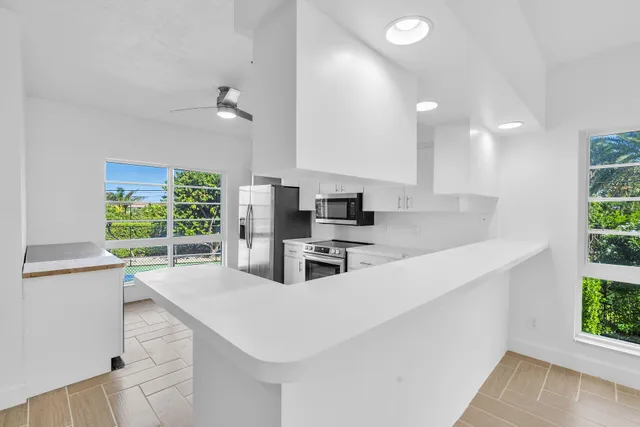 a kitchen with stainless steel appliances a sink a stove a microwave a center island and windows