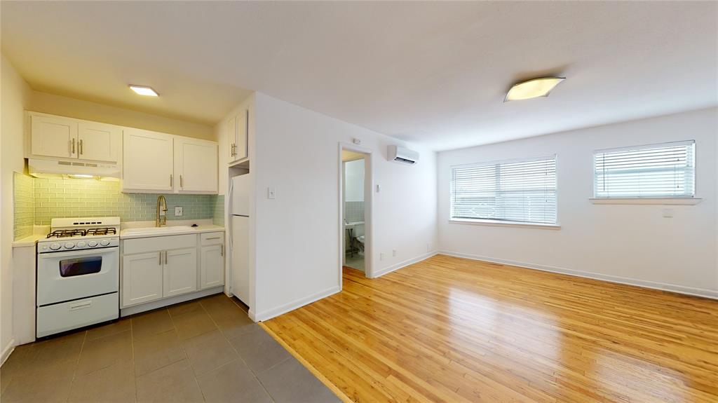Kitchen featuring white appliances, under cabinet range hood, a wall unit AC, decorative backsplash, and light countertops