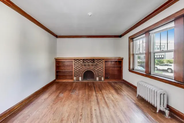a view of an empty room with wooden floor fireplace and a window
