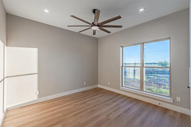 an empty room with wooden floor fan and windows