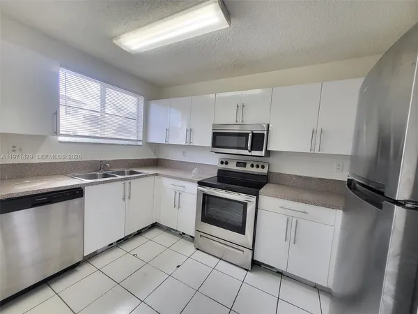 a kitchen with white cabinets appliances and a window