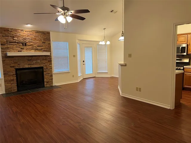 an empty room with wooden floor a ceiling fan a fireplace and windows