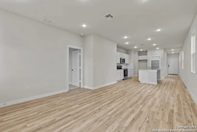 a view of empty room with wooden floor and kitchen