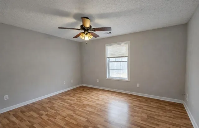an empty room with wooden floor fan and windows