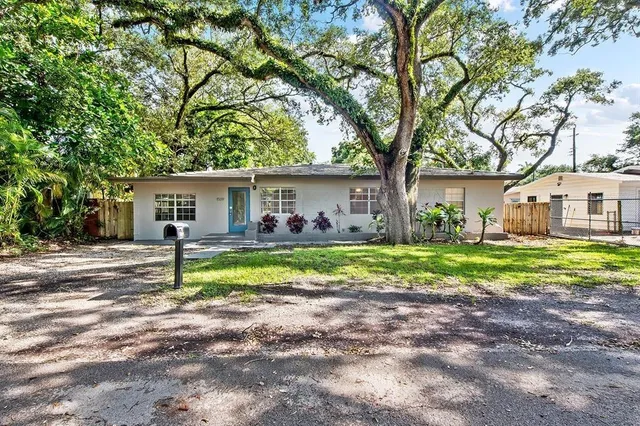 a view of house in front of a big yard with large trees and plants