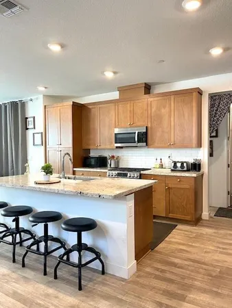 a kitchen with stainless steel appliances granite countertop a stove top oven a sink refrigerator and white cabinets with wooden floor