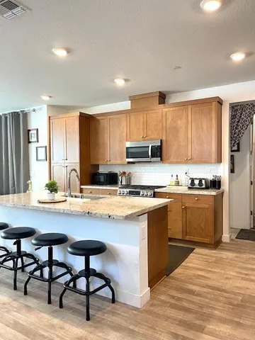 a kitchen with stainless steel appliances granite countertop a stove top oven a sink refrigerator and white cabinets with wooden floor