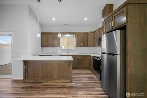 a kitchen with stainless steel appliances granite countertop a refrigerator a stove and a sink with wooden floor