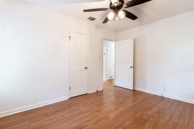 an empty room with wooden floor ceiling fan and windows