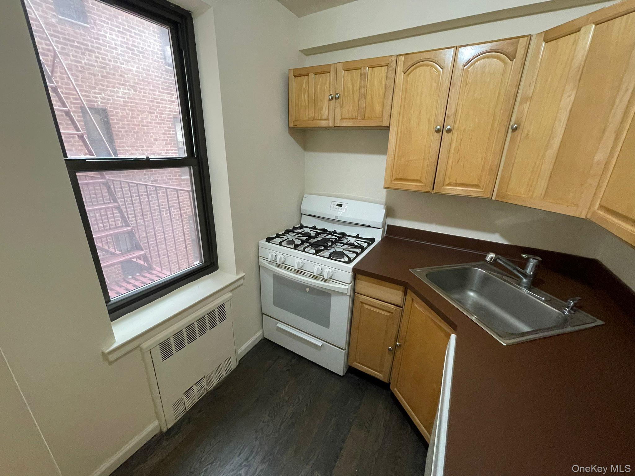100-11 67th Road, Unit 4 Queens, NY 11375 - Photo 18 of 33 Kitchen with white range with gas cooktop, dark countertops, dark wood finished floors, light brown cabinetry, and radiator heating unit