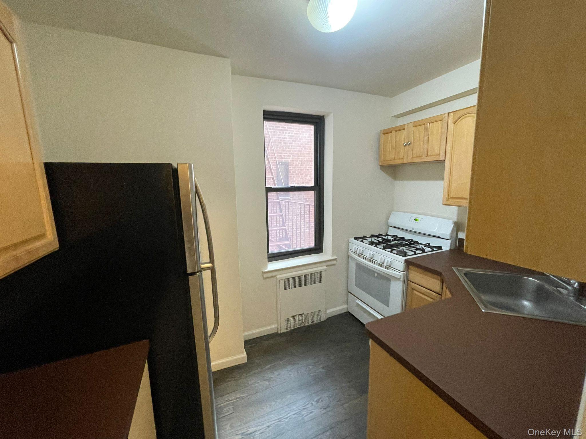 100-11 67th Road, Unit 4 Queens, NY 11375 - Photo 21 of 33 Kitchen with white gas range oven, light brown cabinets, dark countertops, freestanding refrigerator, and radiator