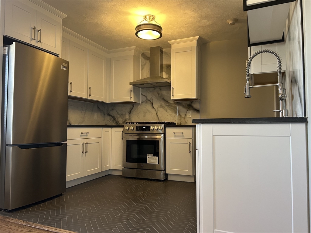 18 Ashcroft Street, Unit 301 Dedham, MA 02026 - Photo 4 of 14 a kitchen with stainless steel appliances granite countertop a refrigerator a stove and a sink with wooden floor