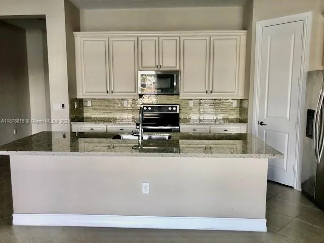 a view of kitchen with stainless steel appliances granite countertop a stove a refrigerator and a white cabinets