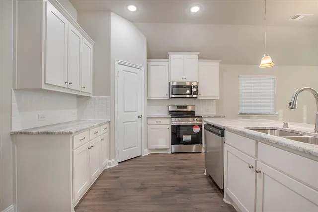 an empty room with wooden floor and kitchen view