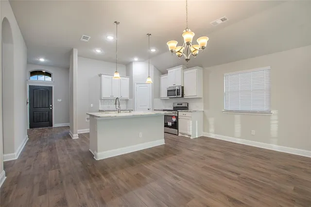 an empty room with wooden floor chandelier and windows