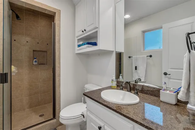 a bathroom with a granite countertop sink a toilet a mirror and shower