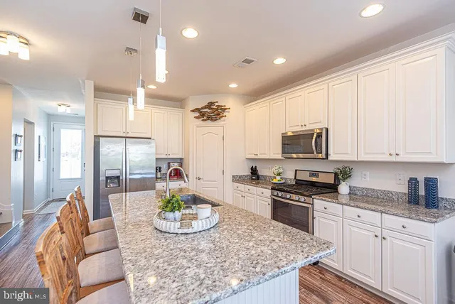 a kitchen with stainless steel appliances granite countertop a stove top oven a sink dishwasher a dining table and chairs with wooden floor