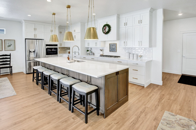 910 South 1700 West Layton, UT 84041 - Photo 4 of 26 Two tone kitchen with two tone cabinets, stainless steel appliances, a large island with sink, light wood finished floors, and light stone countertops