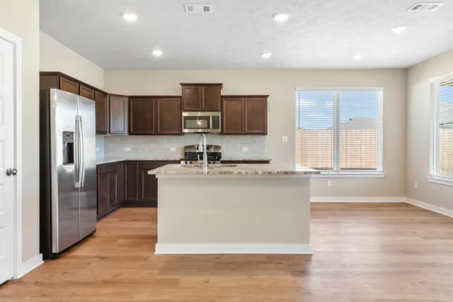 a large kitchen with stainless steel appliances wooden floor and a window