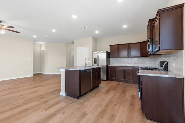 a kitchen with stainless steel appliances granite countertop a sink a stove a refrigerator cabinets and wooden floor