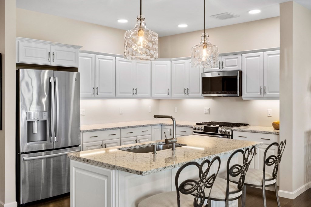 1 Revolution Way, Unit 201 Canton, MA 02021 - Photo 8 of 38 a kitchen with stainless steel appliances granite countertop a refrigerator a stove a sink a dining table and chairs with wooden floor