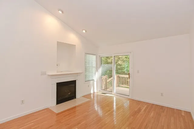 a view of an empty room with wooden floor fireplace and a window