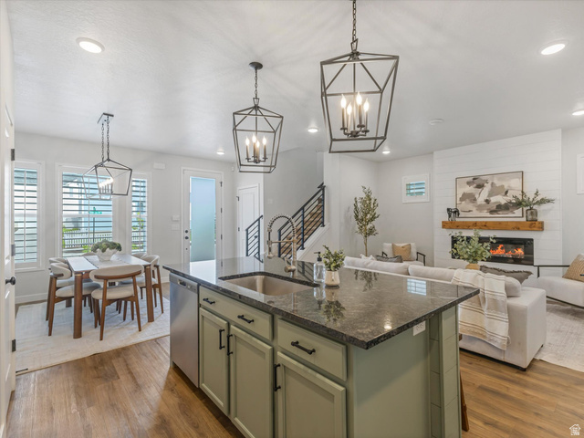 11759 South Watercourse Road South Jordan, UT 84009 - Photo 7 of 33 Open-concept living space featuring a kitchen island with dark countertops, wood-finish flooring, a dining area with multiple windows, a living room with a shiplap fireplace, and a staircase with metal railings