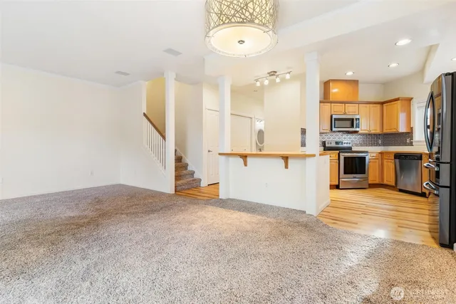 an empty room with wooden floor and way to kitchen
