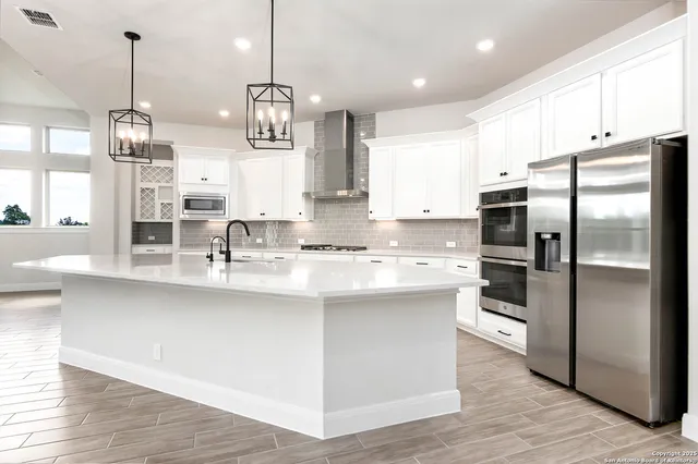 a kitchen with stainless steel appliances granite countertop a refrigerator a sink dishwasher a stove and white cabinets with wooden floor