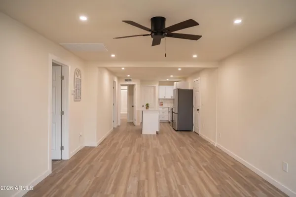 a view of a big room with wooden floor a ceiling fan and kitchen space