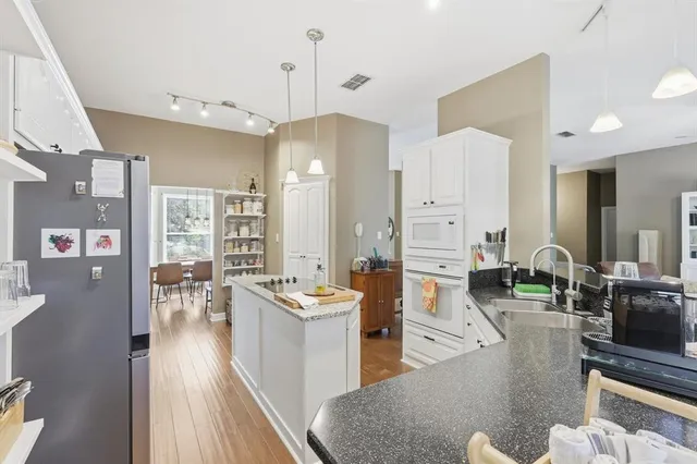 a living room with stainless steel appliances kitchen island granite countertop a couch a dining table and chairs with wooden floor