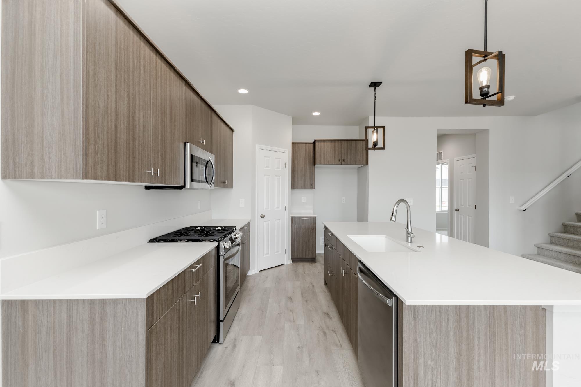 12842 Ropers Street Nampa, ID 83651 - Photo 4 of 29 Modern kitchen featuring wood-grain cabinetry, stainless steel appliances, and a spacious island with an integrated sink