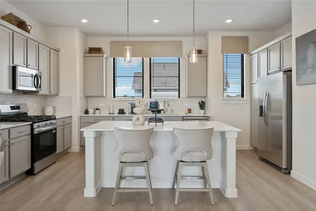 a kitchen with stainless steel appliances granite countertop a stove a sink a refrigerator a microwave oven with white cabinets and wooden floor