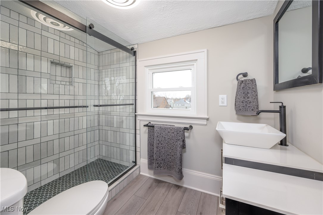 17728 Windward Road Cleveland, OH 44119 - Photo 18 of 32 Bathroom featuring vanity, an enclosed shower, wood-type flooring, a textured ceiling, and toilet
