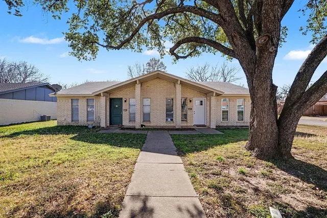 a view of a white house with a large tree and plants