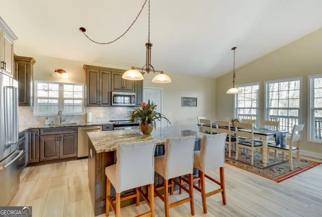 a kitchen with stainless steel appliances granite countertop a stove a sink a refrigerator a dining table and chairs with wooden floor