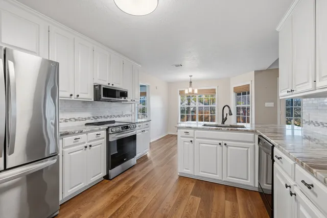 a kitchen with white cabinets stainless steel appliances and wooden floor