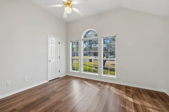 an empty room with wooden floor fan and windows