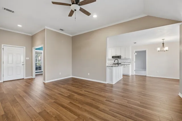 a view of an empty room with wooden floor and a kitchen