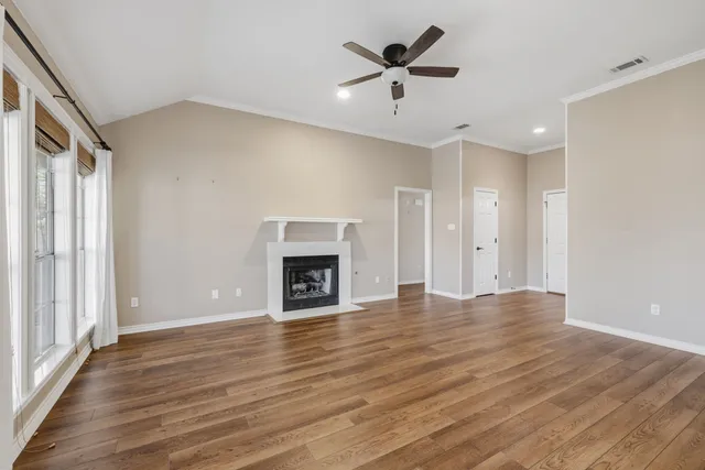 an empty room with wooden floor a ceiling fan a fireplace and windows