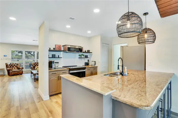 a kitchen with granite countertop a sink a stove top oven a chimney and living room view