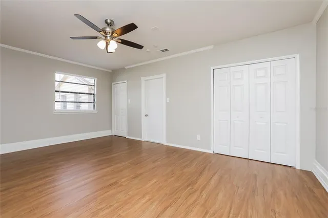 an empty room with wooden floor chandelier fan and windows