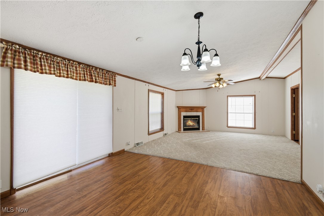60602 Shaw Road Cambridge, OH 43725 - Photo 14 of 41 Unfurnished living room with crown molding, wood finished floors, a tiled fireplace, carpet, and a chandelier