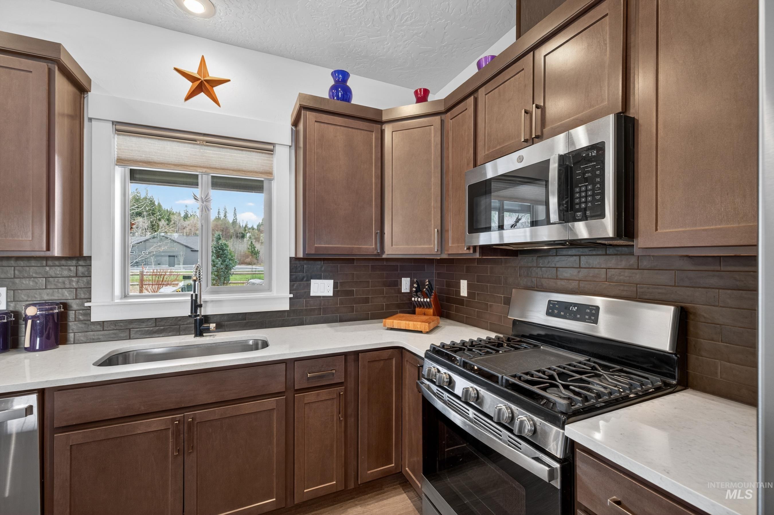 1126 Mo's Way McCall, ID 83638 - Photo 13 of 50 Kitchen featuring wood-finish cabinetry, stainless steel appliances, solid surface countertops, a rectangular undermount sink with a matte black faucet, and a horizontally stacked tile backsplash