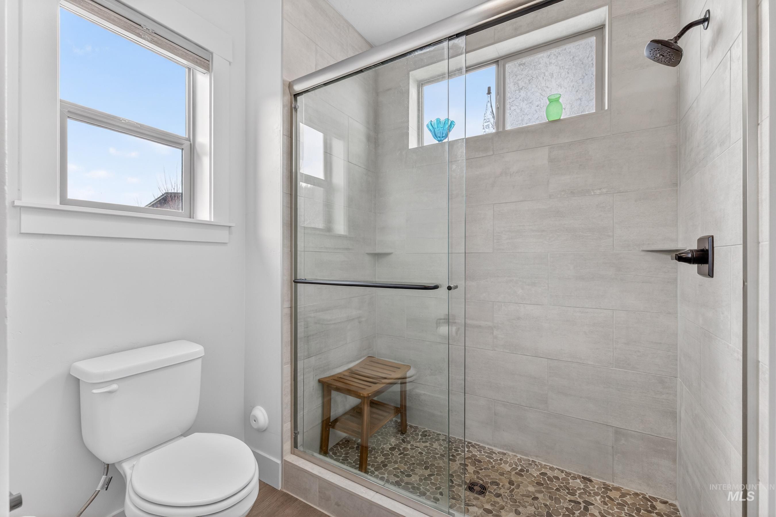 1126 Mo's Way McCall, ID 83638 - Photo 28 of 50 Glass-enclosed shower featuring a dark bronze rainfall showerhead, pebble tile flooring, and light gray large format wall tiles