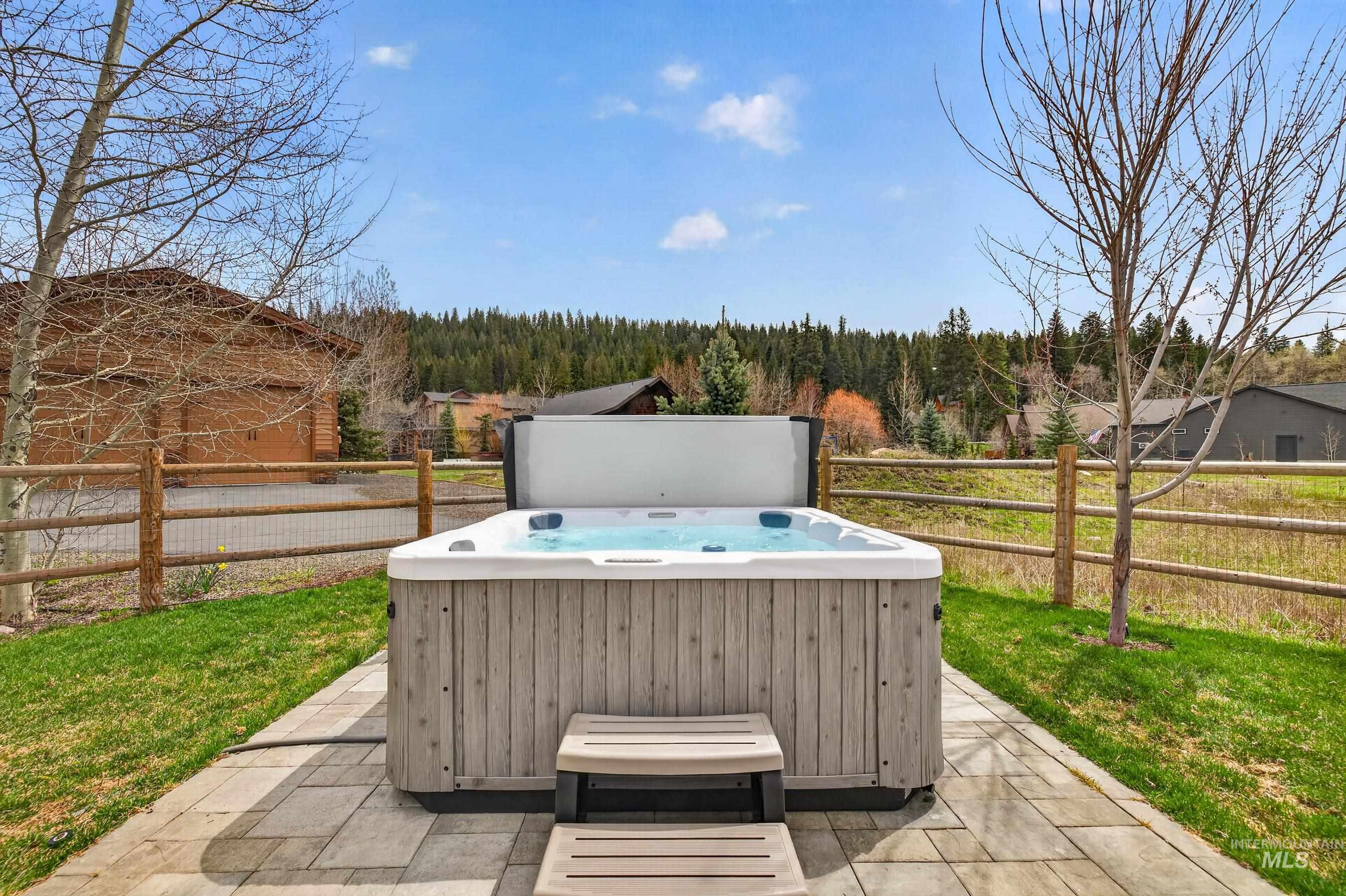 1126 Mo's Way McCall, ID 83638 - Photo 39 of 50 Outdoor spa on a paver patio with steps, surrounded by green lawn and a split-rail fence