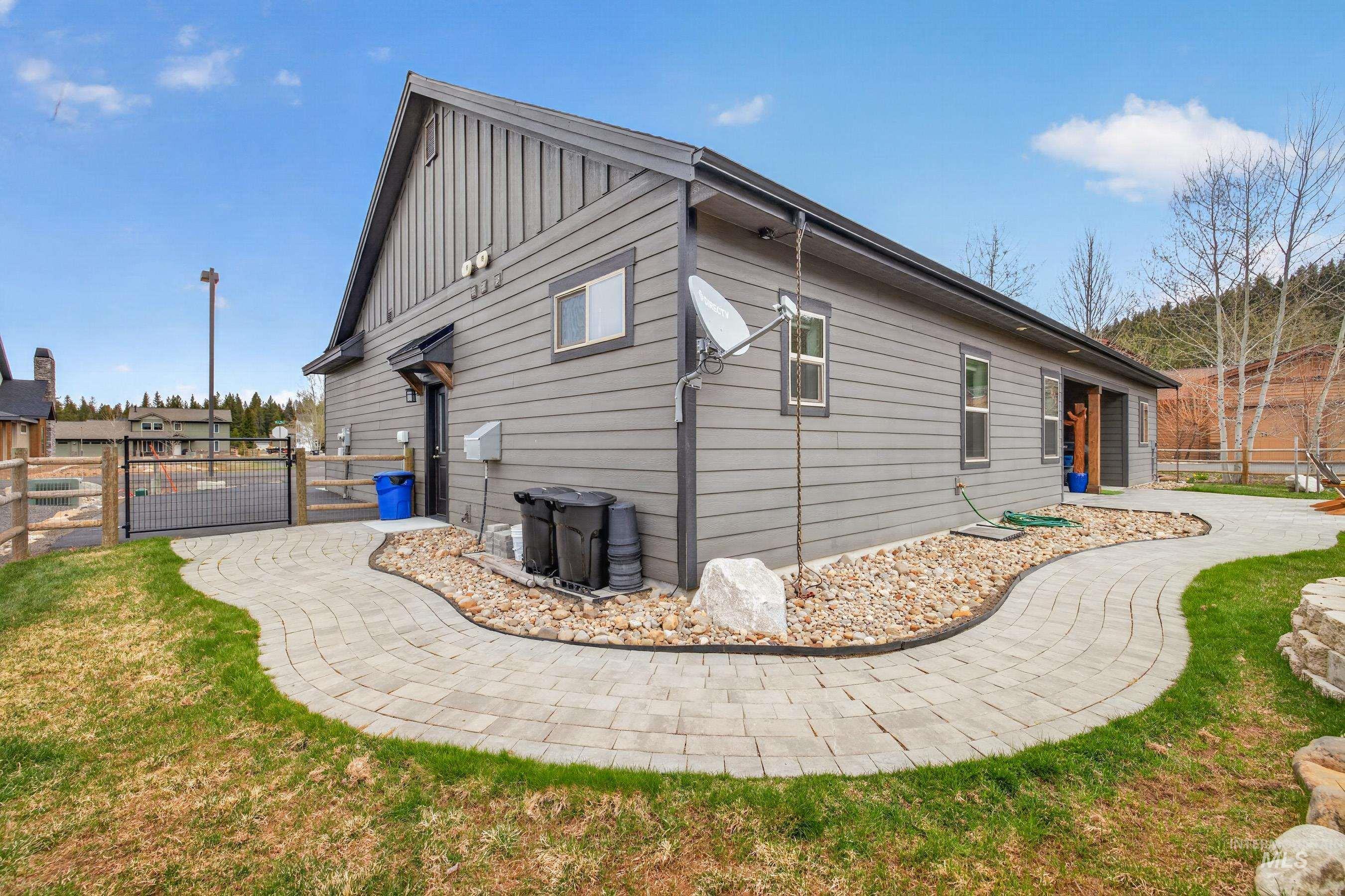 1126 Mo's Way McCall, ID 83638 - Photo 43 of 50 Contemporary exterior with horizontal siding and vertical accent panels, featuring a paved walkway, rock landscaping, and a fenced yard area