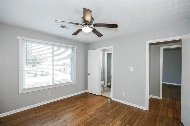 a view of an empty room with wooden floor and a ceiling fan